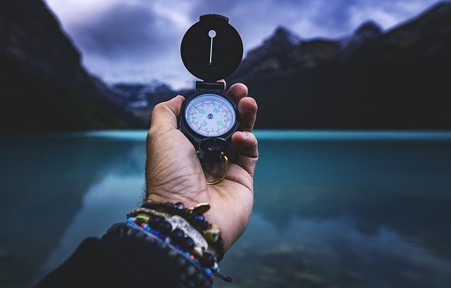 hand holding a compass up to a backdrop of moody mountains